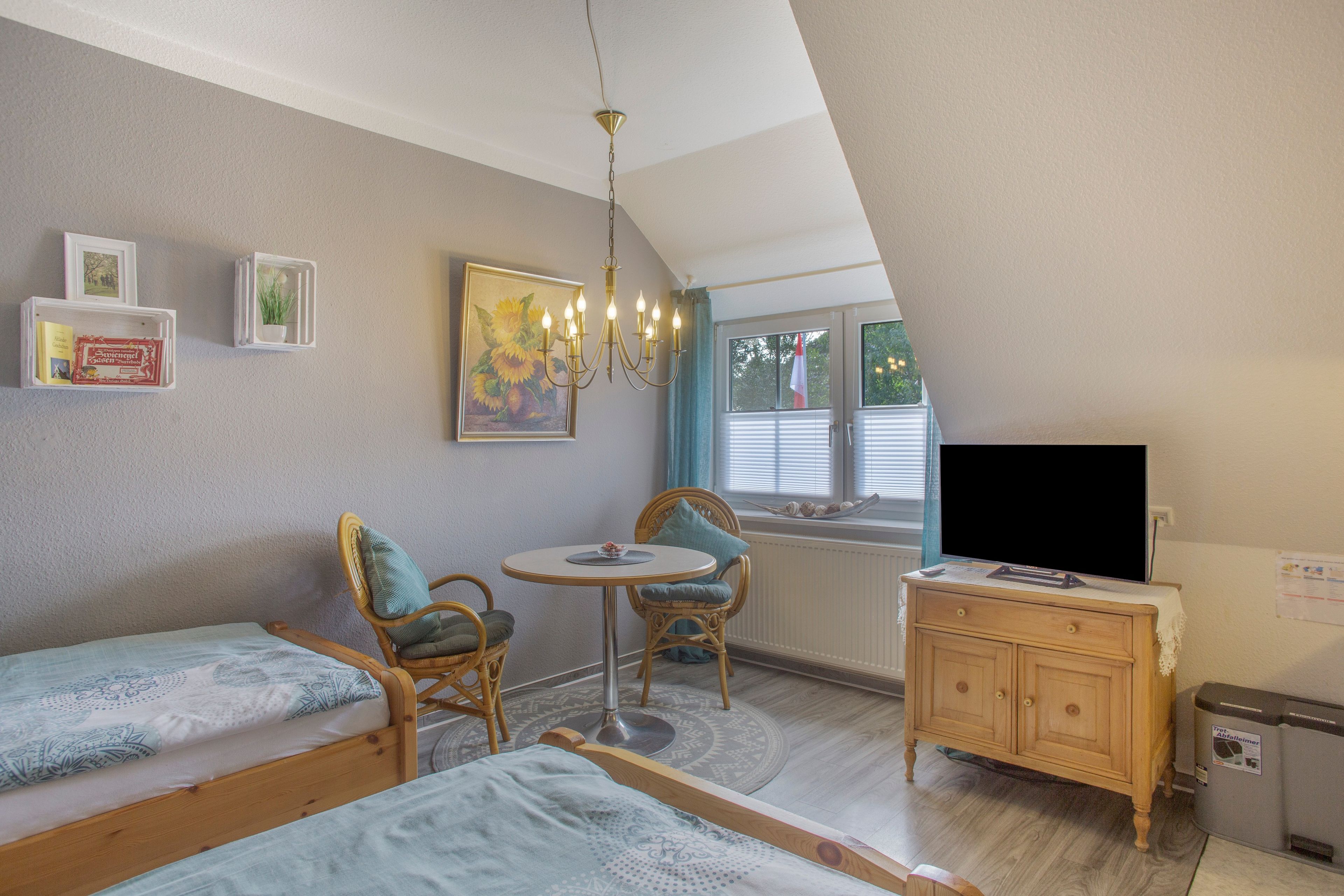 A cozy room with a bed, a small table with chairs, a TV, and a painting on the wall.