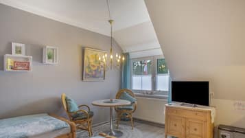 A cozy room with a bed, a small table with chairs, a TV, and a painting on the wall.