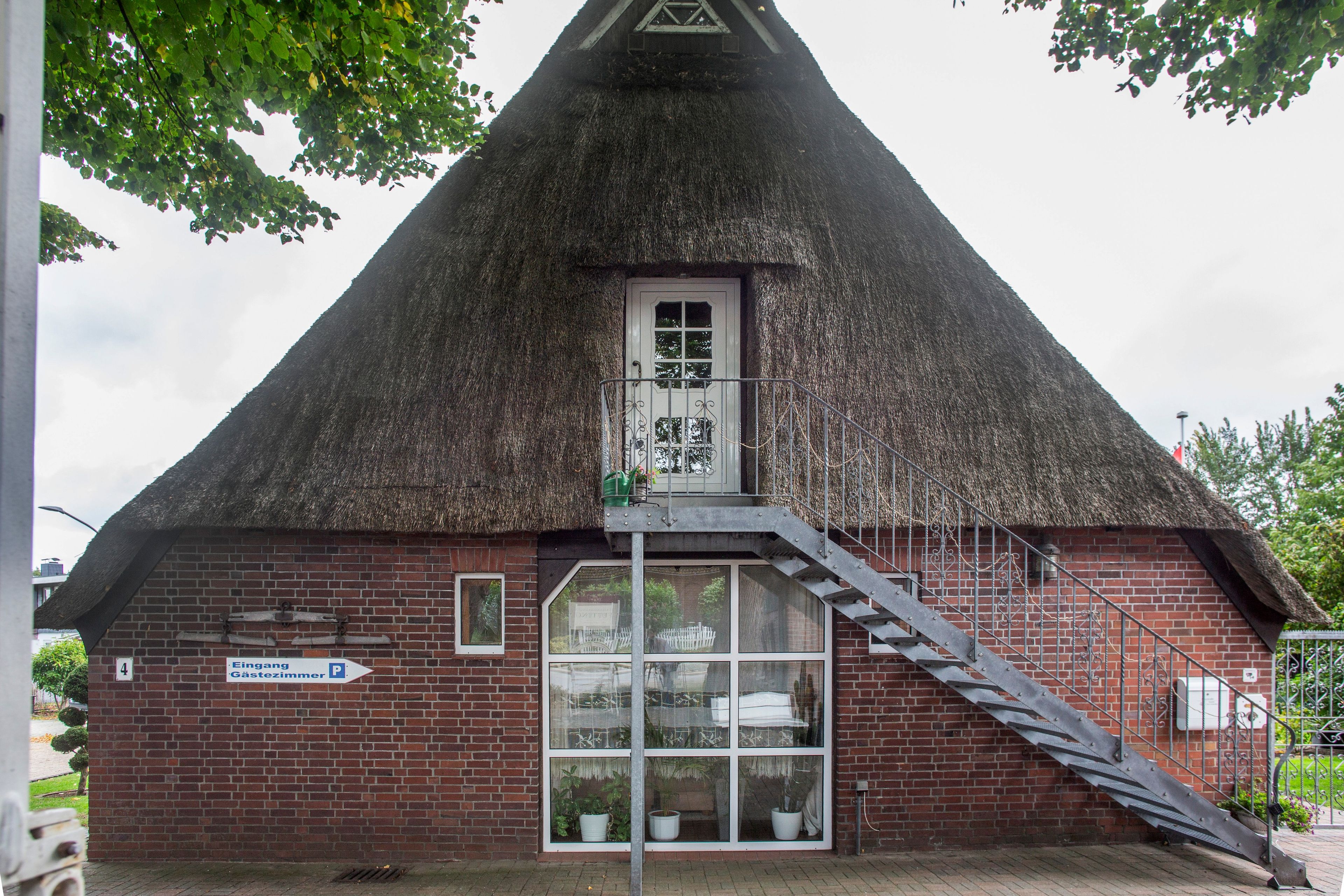 Un bâtiment traditionnel avec un toit de chaume, un escalier menant à une porte et une enseigne indiquant une chambre d’hôtes.