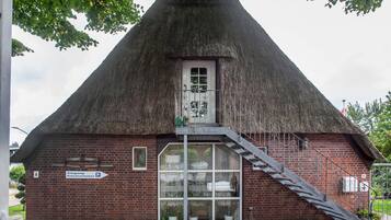 Ein traditionelles Gebäude mit einem Reetdach, einer Treppe, die zu einer Tür führt, und einem Schild, das ein Gästezimmer anzeigt.