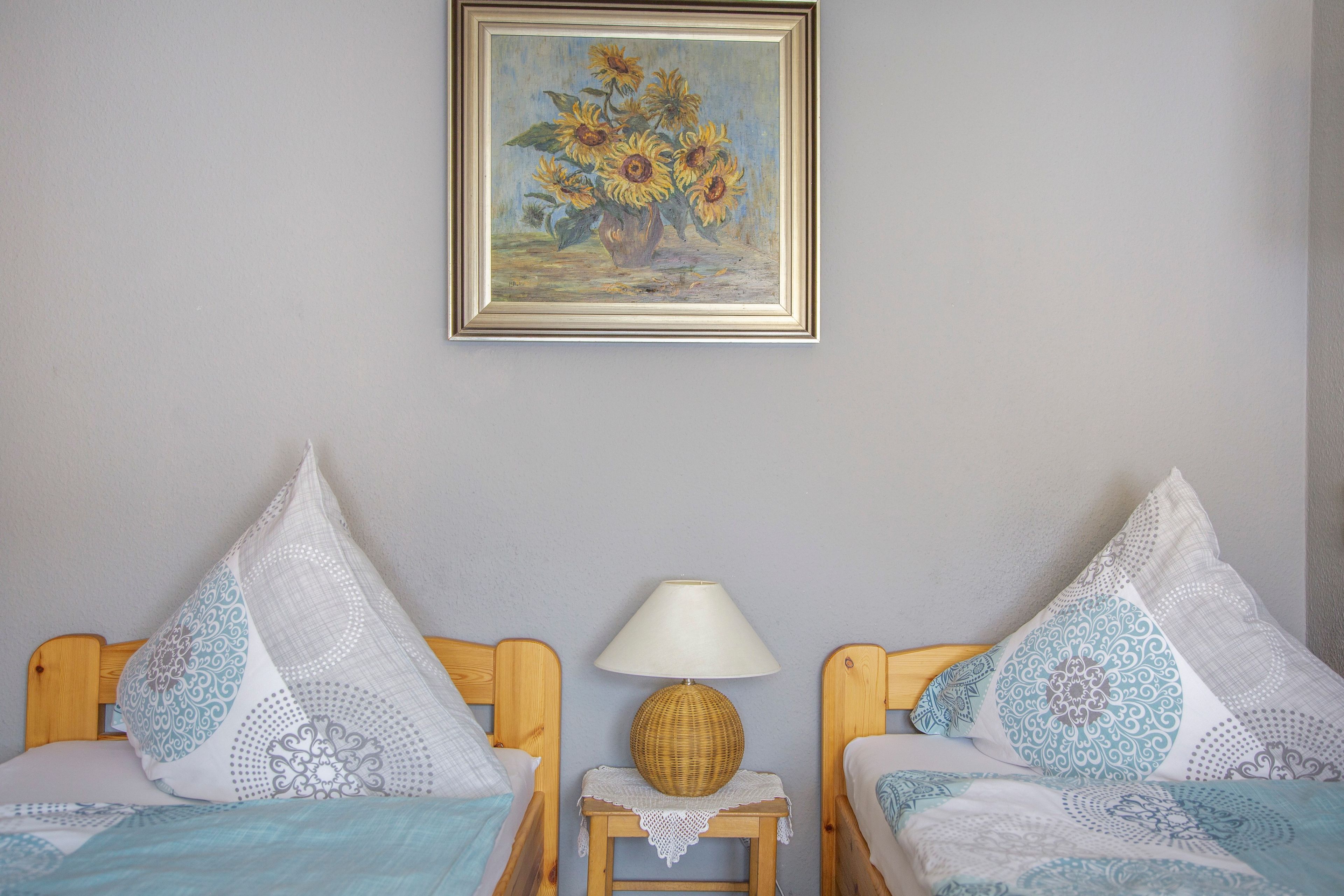 Une chambre avec deux lits, une table de chevet avec une lampe et un tableau encadré au mur.