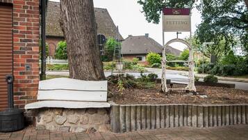 A brick building with a white bench, a tree, and a sign for 'Fetting' in front of a residential area.
