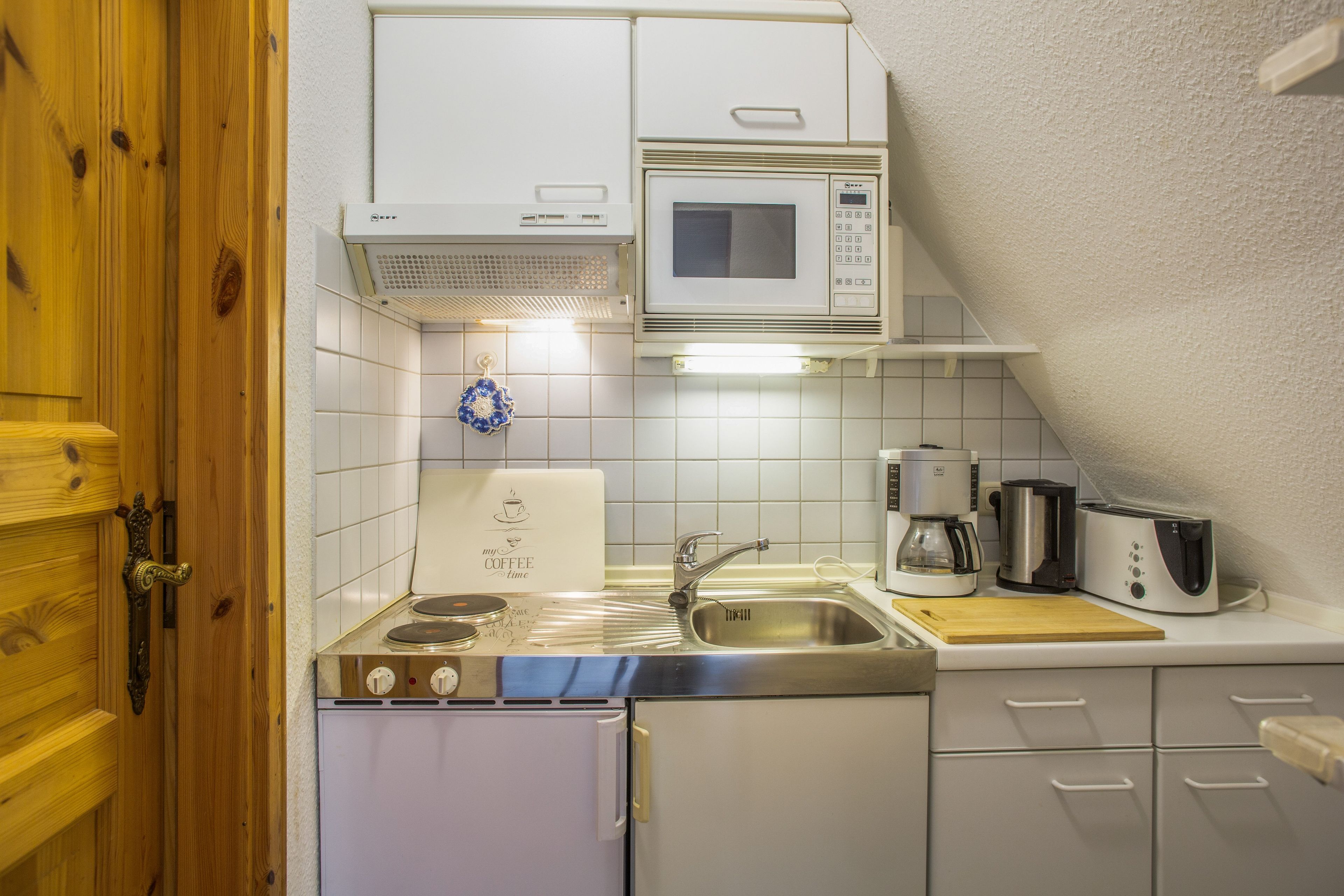 Kompakti keittiö, jossa on mikroaaltouuni, kahvinkeitin ja pieni pesuallas.