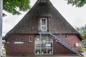 Ein traditionelles Gebäude mit einem Reetdach, einer Treppe, die zu einer Tür führt, und einem Schild, das ein Gästezimmer anzeigt.