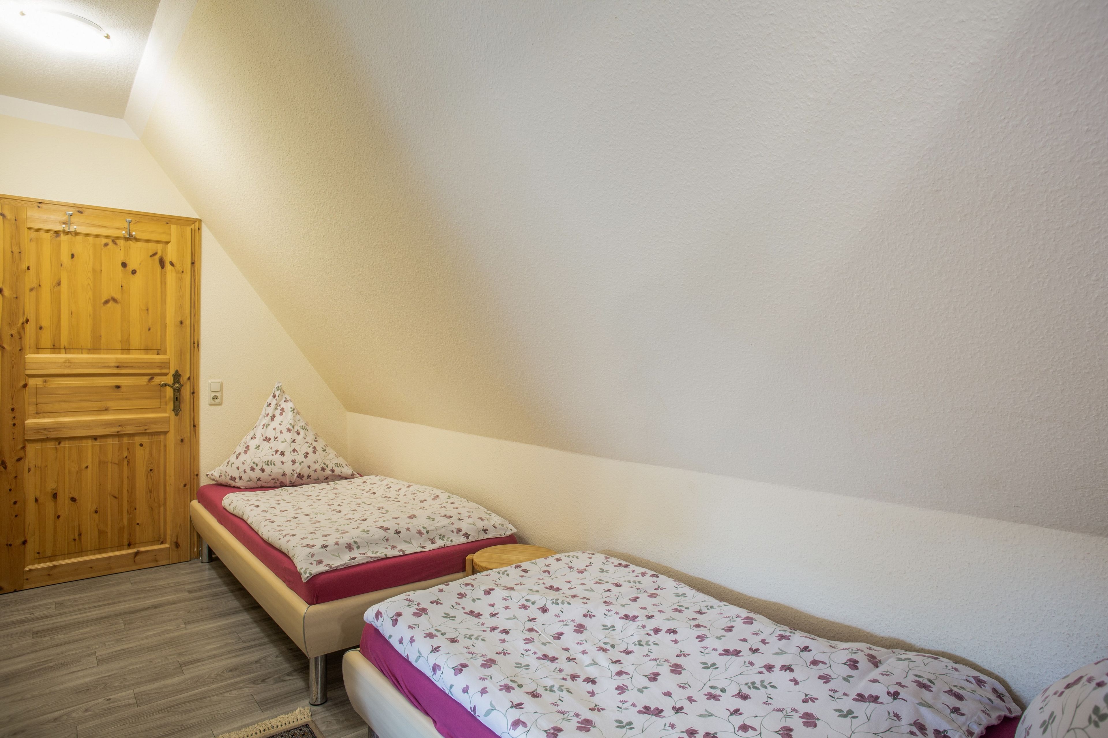 A bedroom with two beds, a wooden wardrobe, and a door.