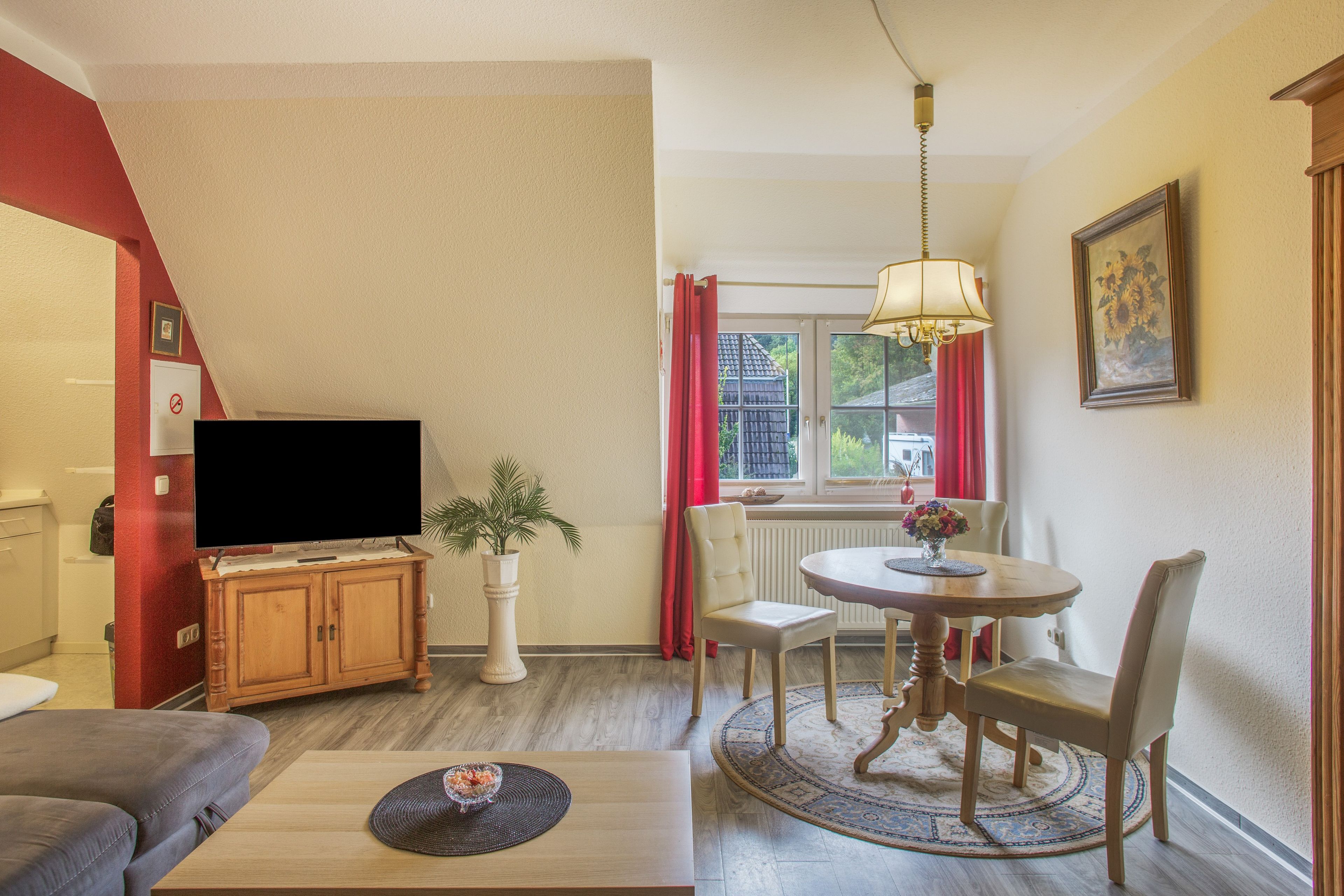 Un salon comprenant une télévision, un canapé, une table basse, une table à manger avec des chaises, une plante en pot et une fenêtre avec des rideaux.