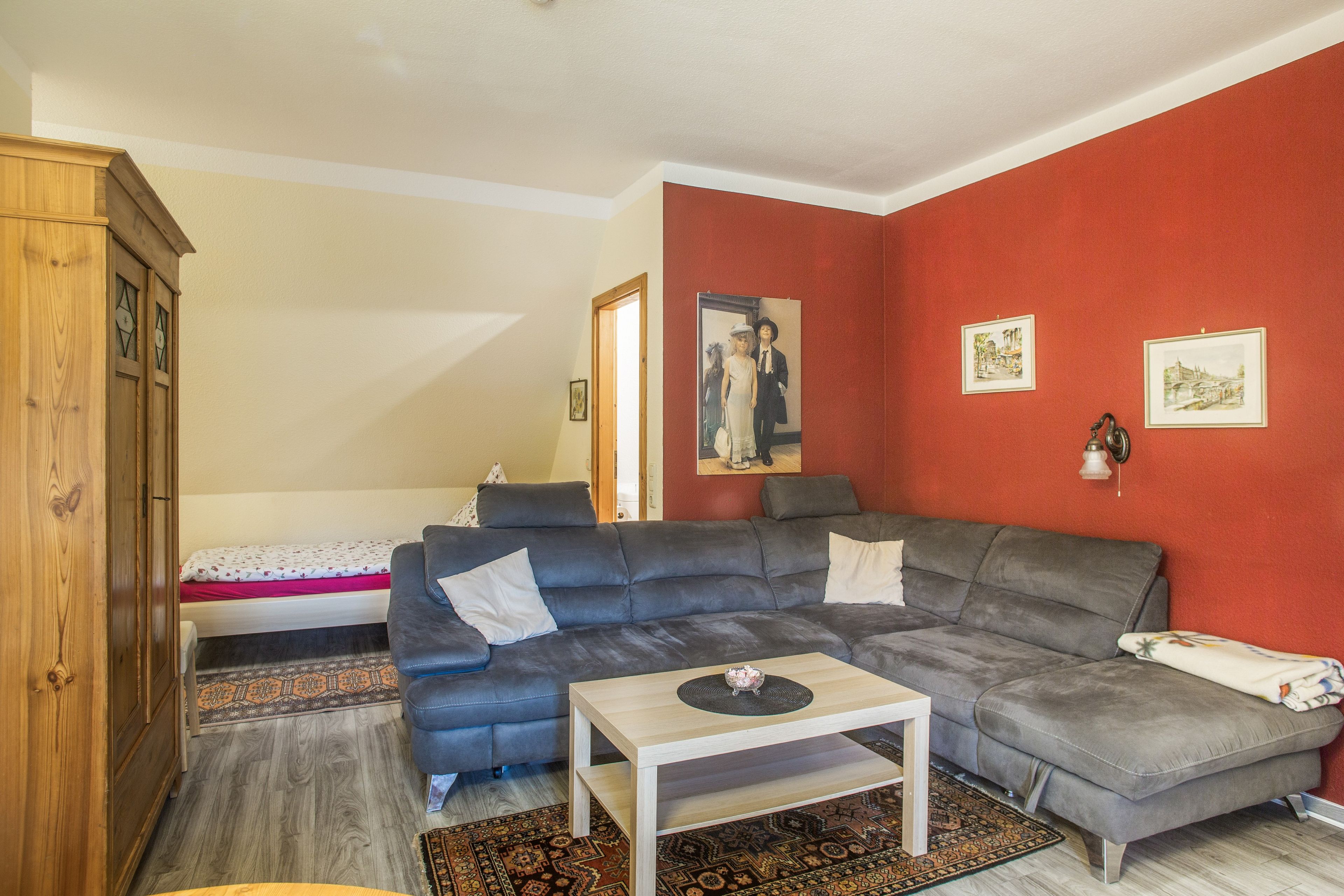 A living room with a grey sofa, a small white table, and a red accent wall.
