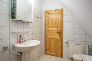 Ein Badezimmer mit Holztür, Waschbecken, Spiegel und Toilette.