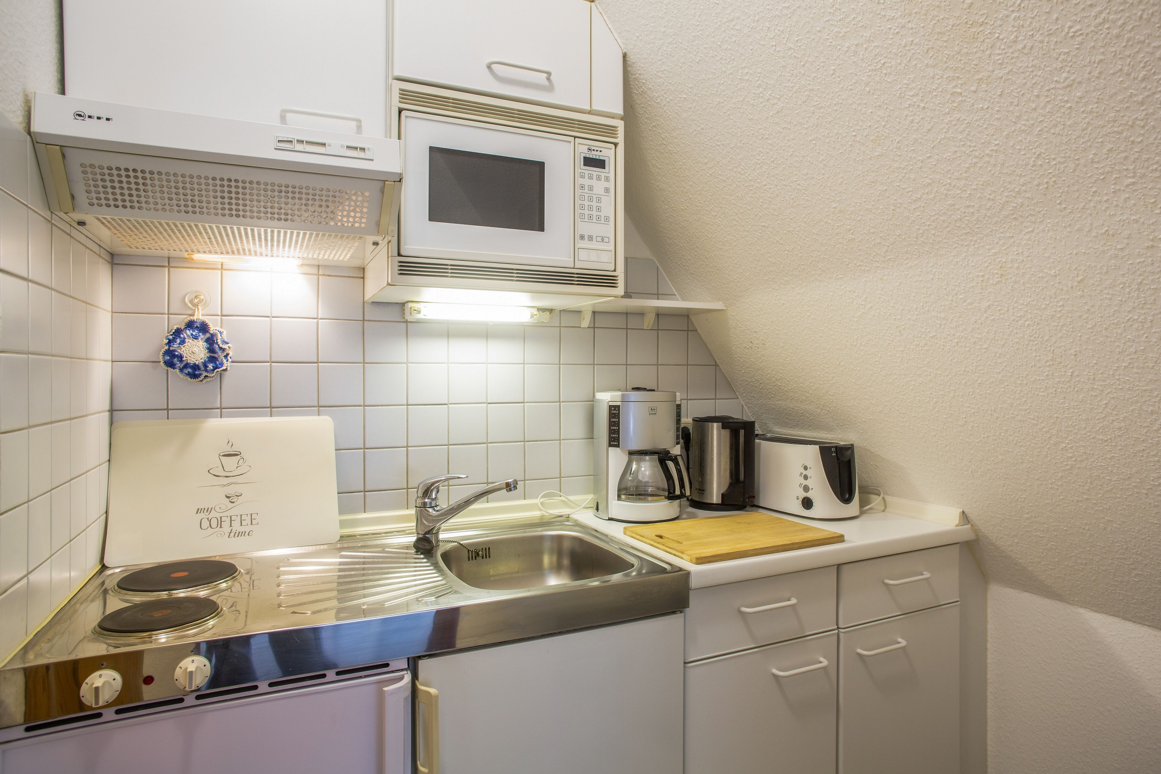 A compact kitchen with a microwave, coffee maker, toaster, and a stove.
