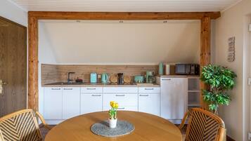 Una cocina con armarios blancos, techo de madera y un comedor con mesa y sillas redondas.