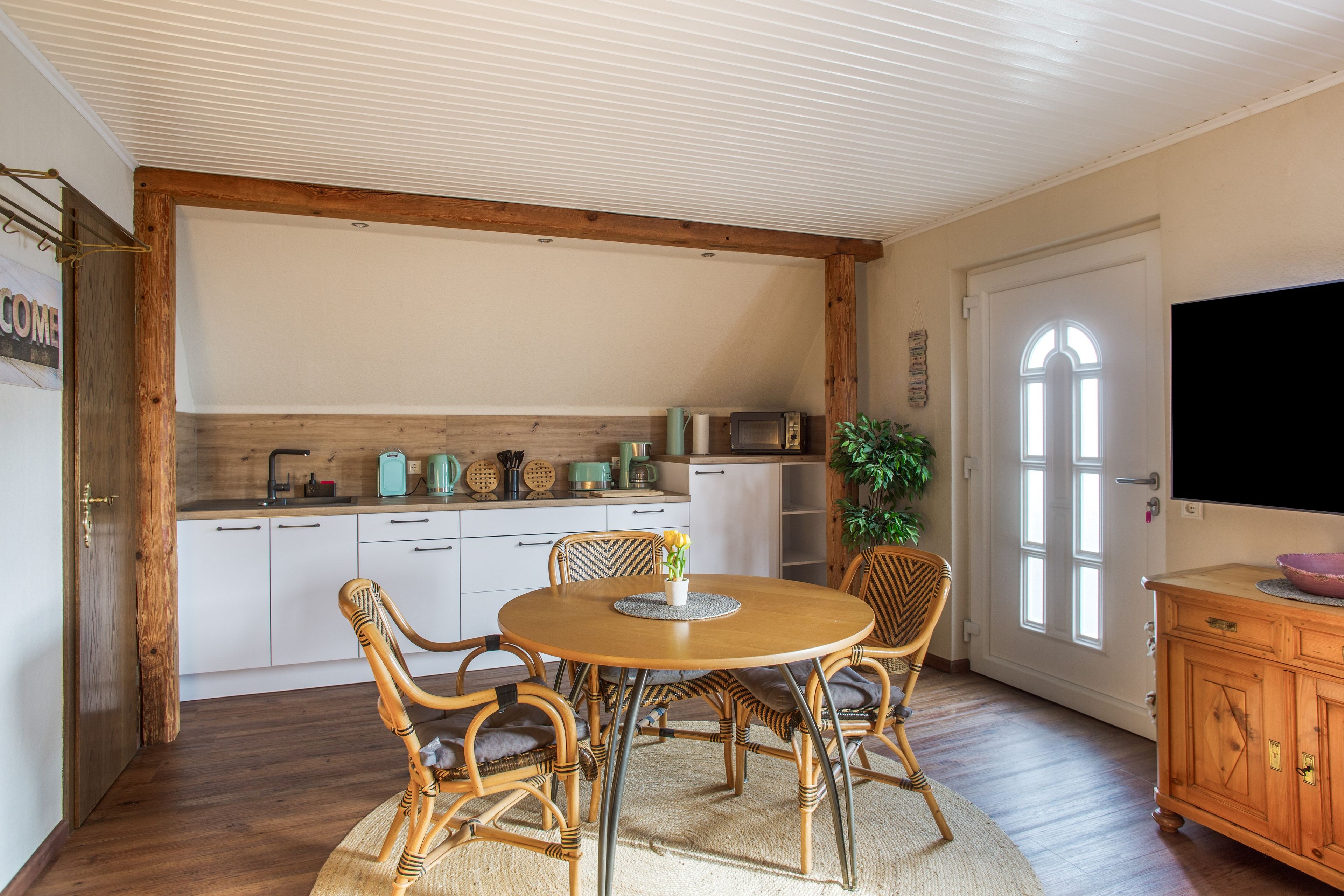 A dining area with a round table, four chairs, and a kitchen in the background.