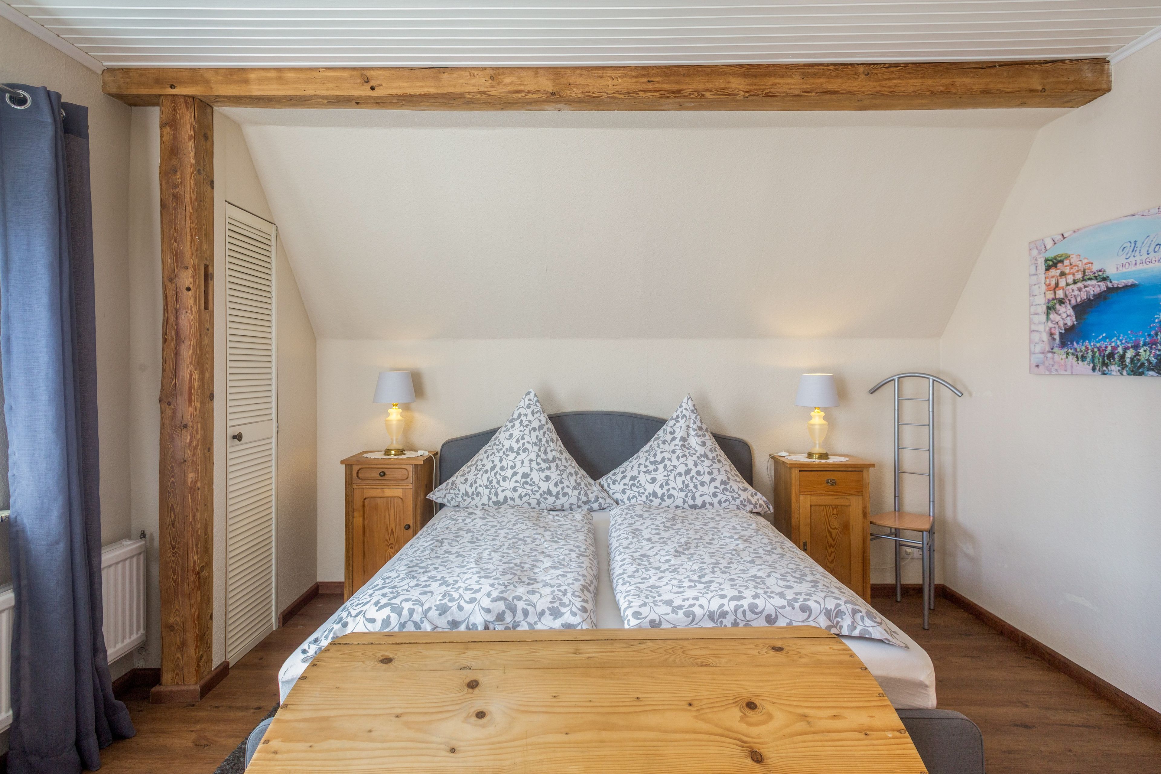 Une chambre avec un lit en bois, deux tables de chevet avec des lampes, une échelle en bois et un tableau au mur.