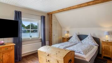 Ein Schlafzimmer mit einem Bett, einem Holz-Kopfteil, Nachttischlampen, einem Schminktisch, einem Fernseher und einem Fenster mit Vorhängen.