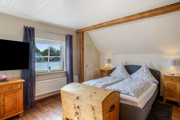 Ein Schlafzimmer mit einem Bett, einem Holz-Kopfteil, Nachttischlampen, einem Schminktisch, einem Fernseher und einem Fenster mit Vorhängen.