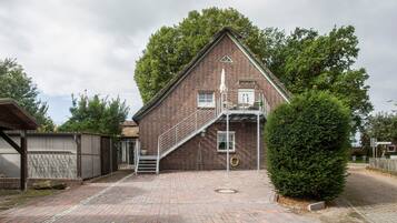 Ein Backsteinhaus mit einer Treppe, die zu einem Balkon führt, umgeben von Bäumen und einem gepflasterten Auffahrt.