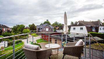 Ein Balkon mit Korbmöbeln, einem weißen Sonnenschirm und Blick auf Häuser und Grünflächen.