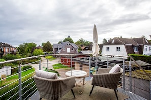 Ein Balkon mit Korbmöbeln, einem weißen Sonnenschirm und Blick auf Häuser und Grünflächen.