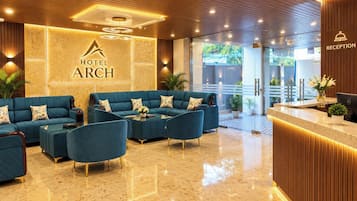 A hotel lobby with a reception desk, a seating area with sofas and armchairs, and a wall with the hotel's name.
