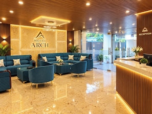 Un hall de hotel con una recepción, un área de descanso con sofás y sillones, y una pared con el nombre del hotel.