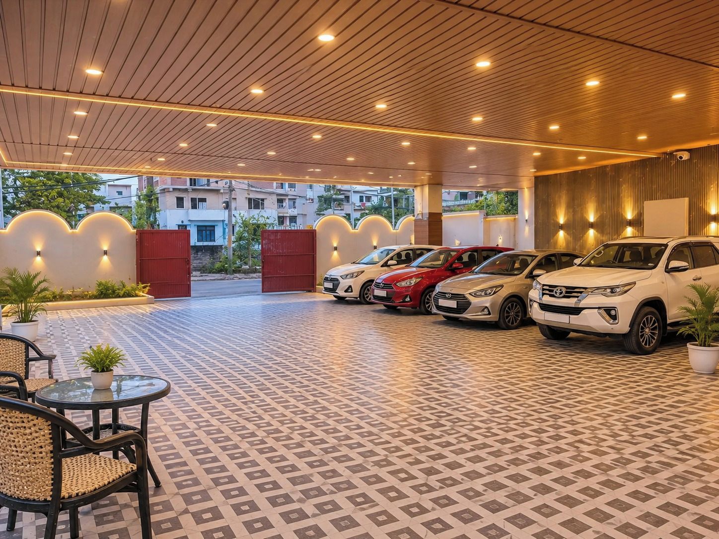 Un área de estacionamiento techada con varios automóviles, piso estampado y un espacio de descanso con mesa y sillas.