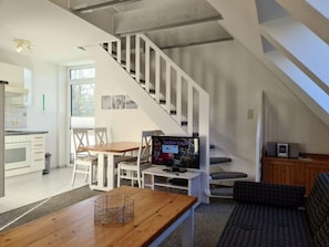 A modern interior with a staircase, a dining area, and a living space with a sofa and television. - Waldstrasse - Holiday Apartment 26 (Wyk auf Foehr)