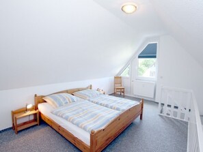 A bedroom with a wooden bed, a nightstand, a chair, and a window. - Waldstrasse - Holiday Apartment 26 (Wyk auf Foehr)