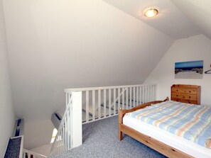 A bedroom with a sloped ceiling, a wooden bed, a dresser, and a painting on the wall. - Waldstrasse - Holiday Apartment 26 (Wyk auf Foehr)