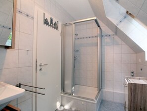 A modern bathroom with a glass-enclosed shower, a white sink, and a wooden vanity. - Waldstrasse - Holiday Apartment 26 (Wyk auf Foehr)