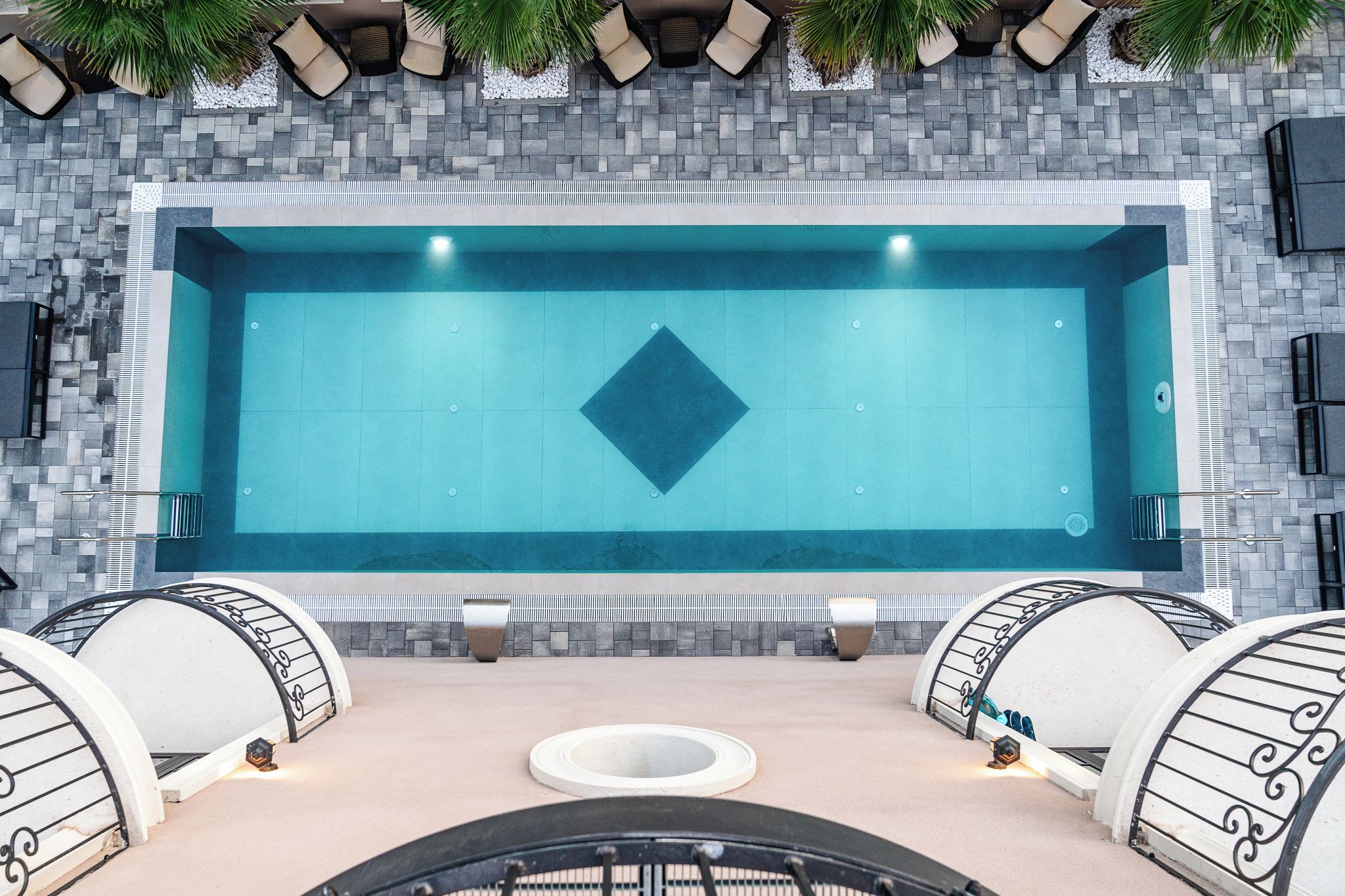 A swimming pool with a geometric tile pattern, surrounded by lounge chairs and a stone wall.