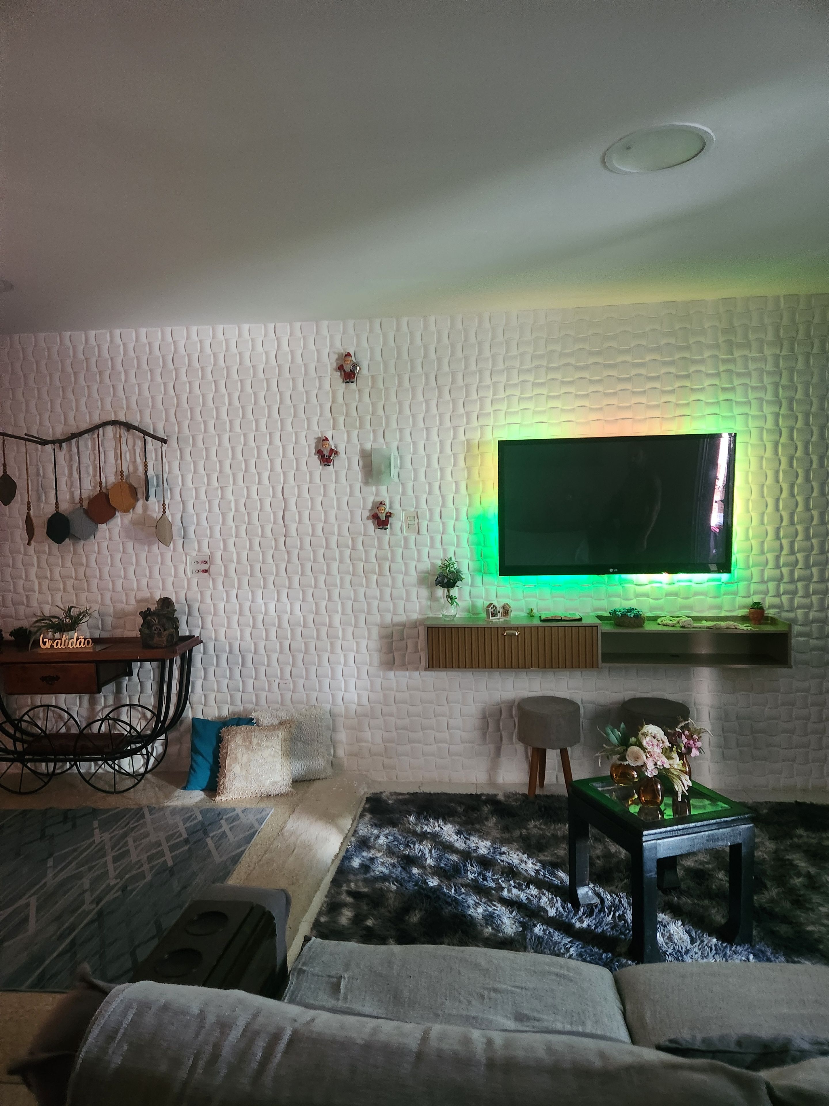 A living room with a flat-screen TV, a sofa, a coffee table with flowers, a decorative wall, and a hanging ornament.