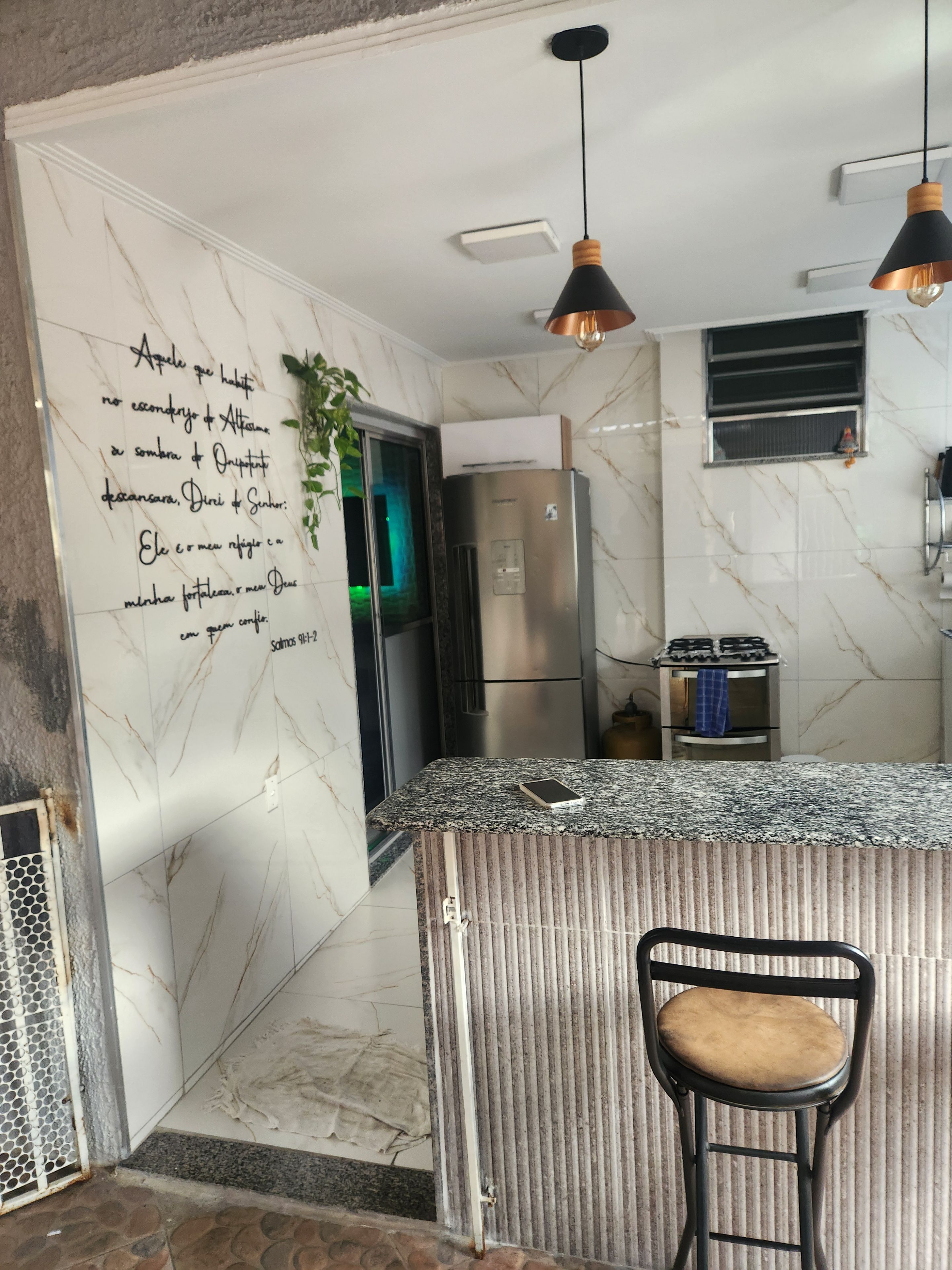 Cocina con salpicadero de mármol, electrodomésticos de acero inoxidable y una zona de bar con una silla.