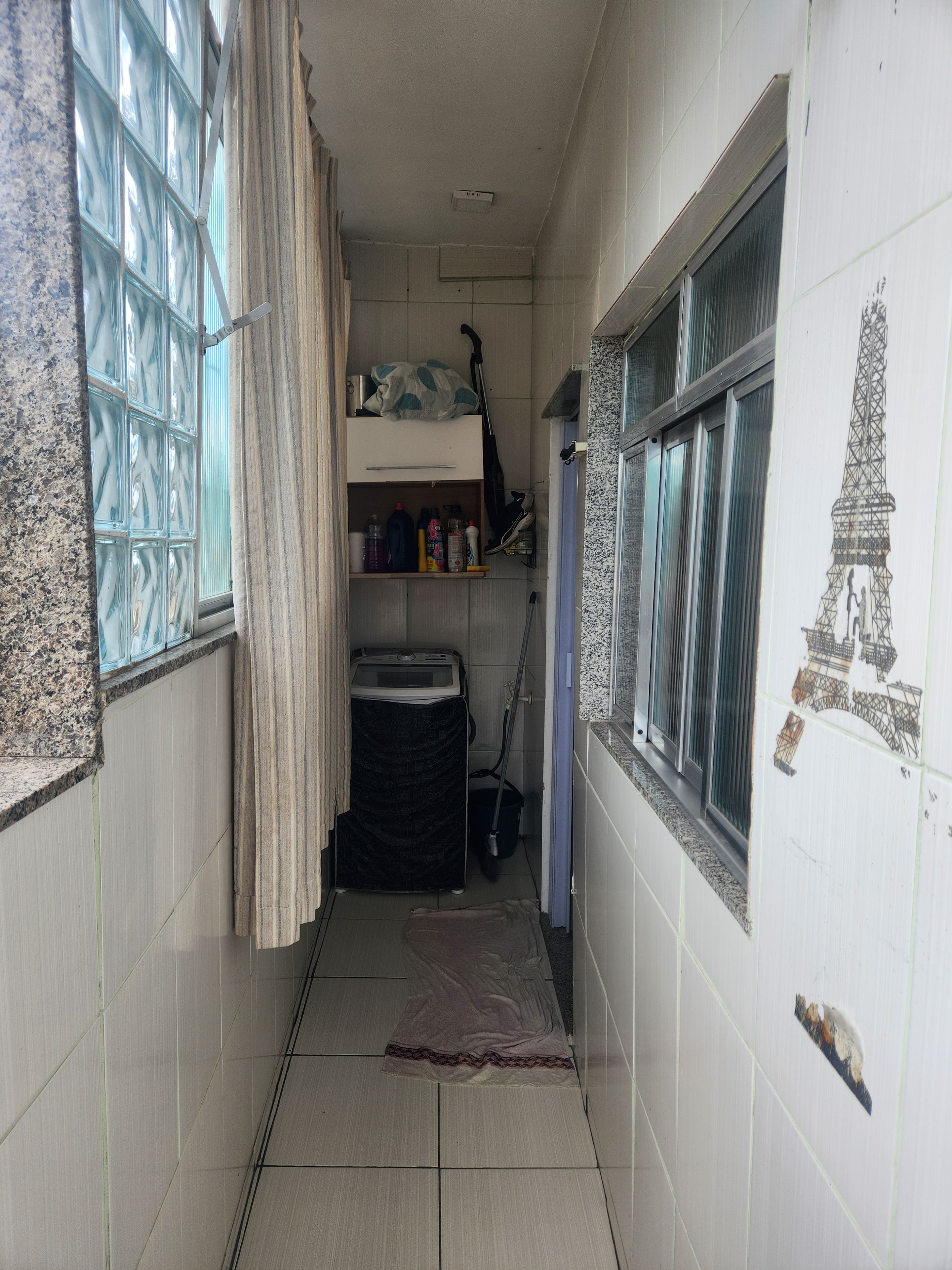 A narrow hallway with a window on one side, a door on the other, and a tiled floor.