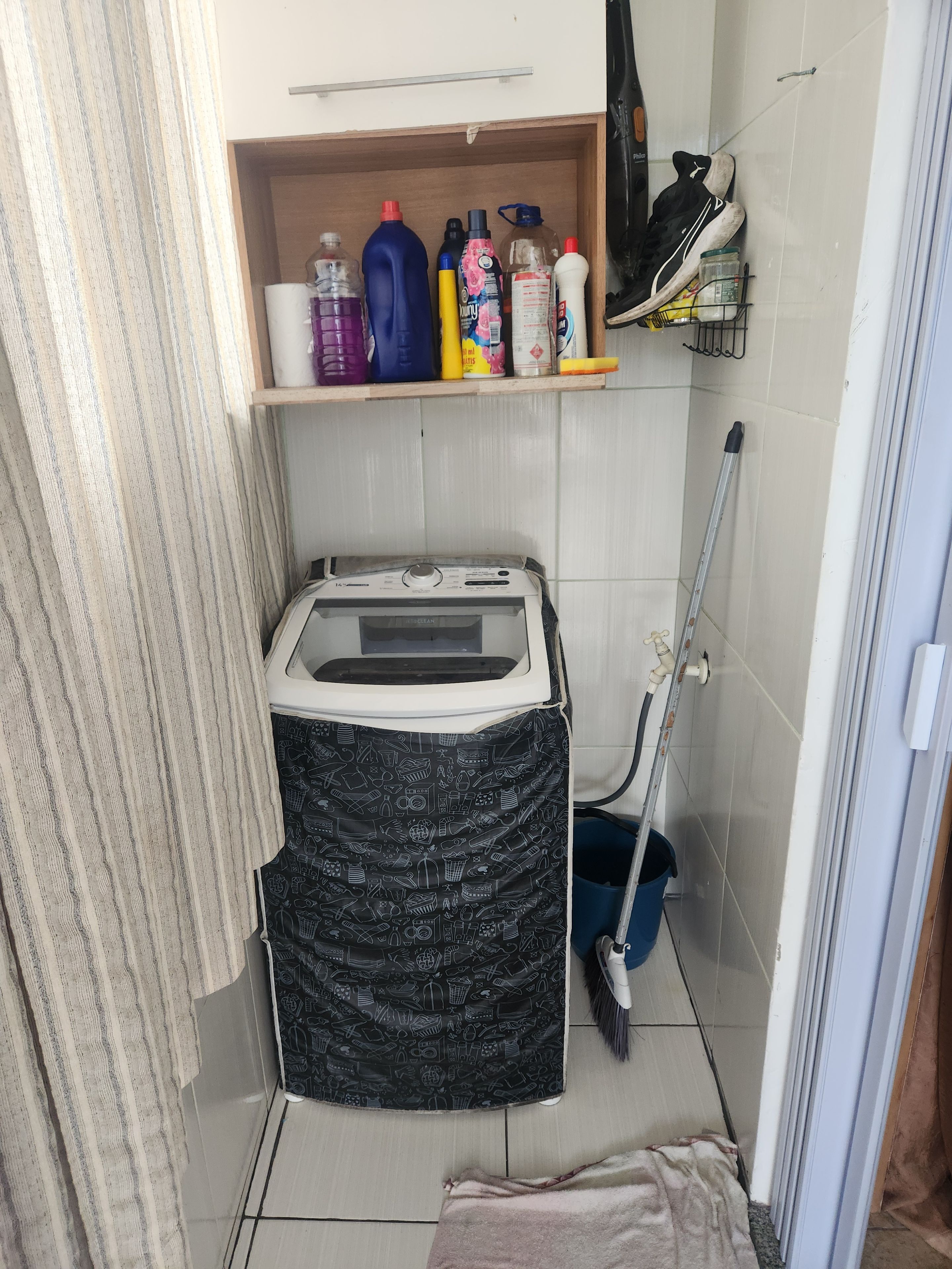 A small bathroom with a toilet, a shower, a shelf with cleaning supplies, and a broom.
