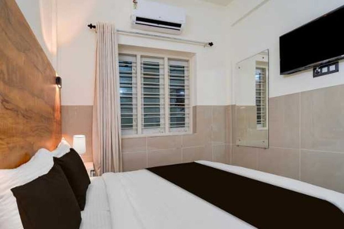 A hotel room with a bed, a TV mounted on the wall, and a window with curtains.