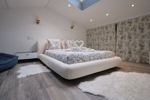 A modern bedroom with a large bed, a nightstand, a blue chair, and a skylight. - New Listing (Aureille)