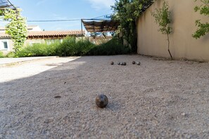 A gravel courtyard with a pergola, a wall with climbing plants, and a building with a tiled roof in the background. - New Listing (Aureille)