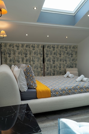 Una camera da letto moderna con un lucernario, tende a motivi, un divano letto con cuscini e un tavolino in marmo.