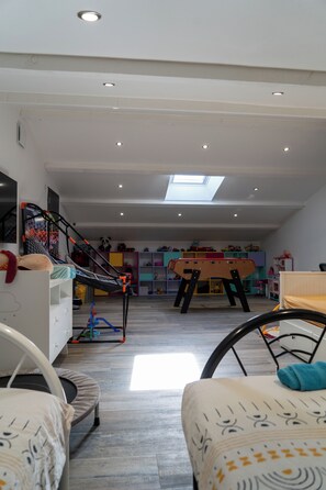 A spacious room with a high ceiling, a skylight, and a play area with a trampoline and toys. - New Listing (Aureille)