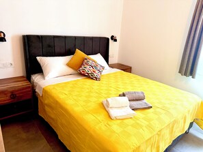 Ein Bett mit gelber Bettdecke, zwei Kissen und zwei gefaltete Handtücher.