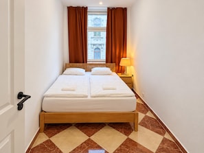 A hotel room with a double bed, a nightstand with a lamp, and a view of a building through the window. - Stay Awhile Vienna 2BR with Living Room (Wien)