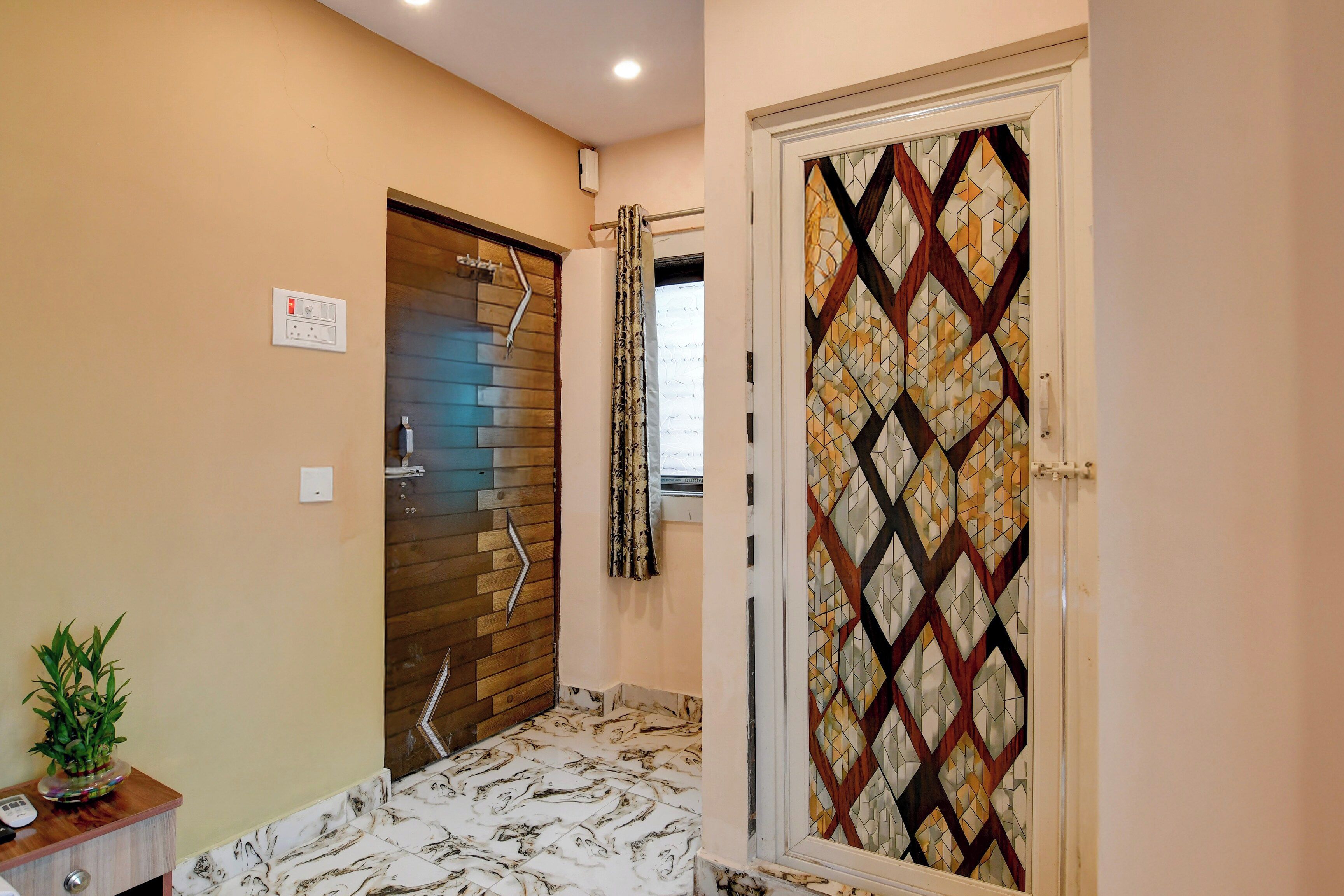 Un baño con puerta de madera, piso de baldosas, planta en maceta y aire acondicionado instalado en la pared.