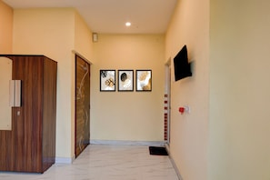 A hallway with a wooden door, a wall-mounted TV, and three framed artworks.