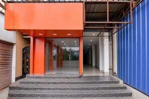 A building entrance with a modern design, featuring a bright orange facade, a set of stairs leading up to the entrance, and a blue wall on the right side.
