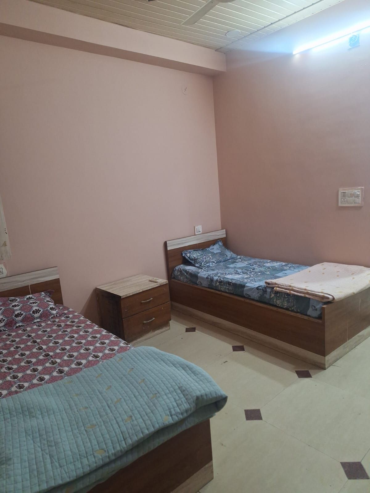 Un dormitorio con dos camas, una mesita de noche e un enchufe de pared.