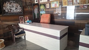 A reception desk with a chair, framed pictures, and a poster on the wall. - CS KHARWAL'S (Pachpadra)