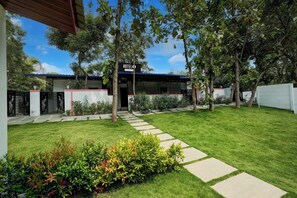 A hotel with a clear pathway leading to the entrance, surrounded by well-maintained greenery and a fenced perimeter.