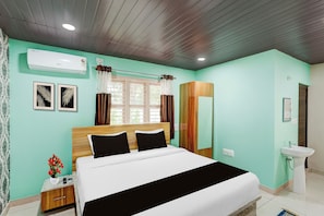 A hotel room with a bed, bedside table, a mirror, a sink, and a window with curtains.