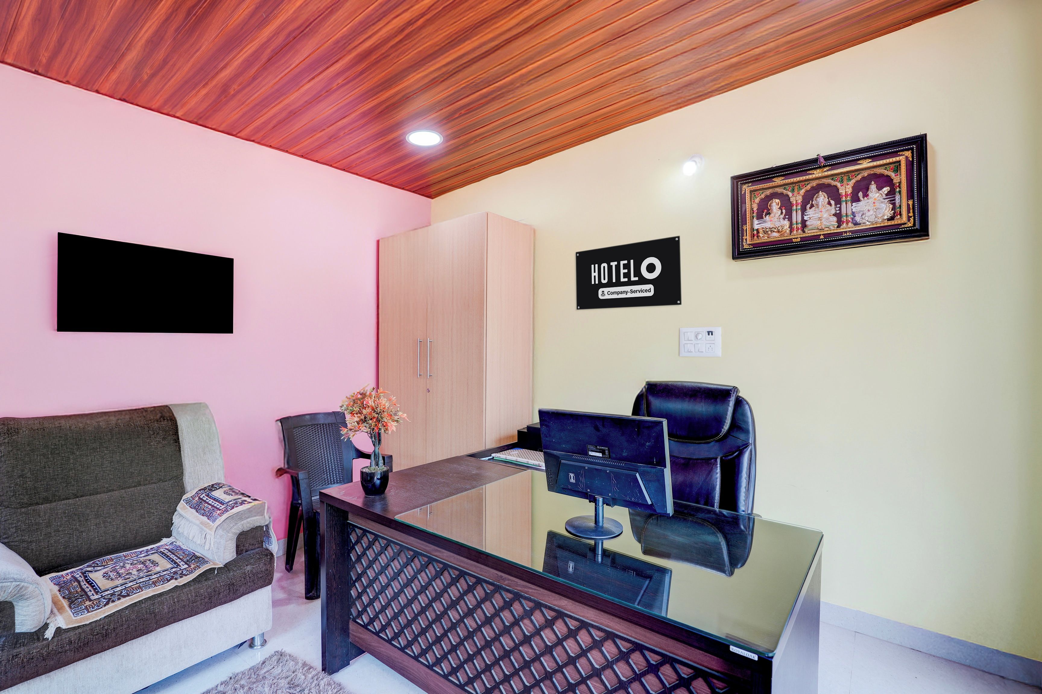 A hotel room with a sofa, a desk with a computer, a chair, a cabinet, and a sign indicating the room is company-serviced.