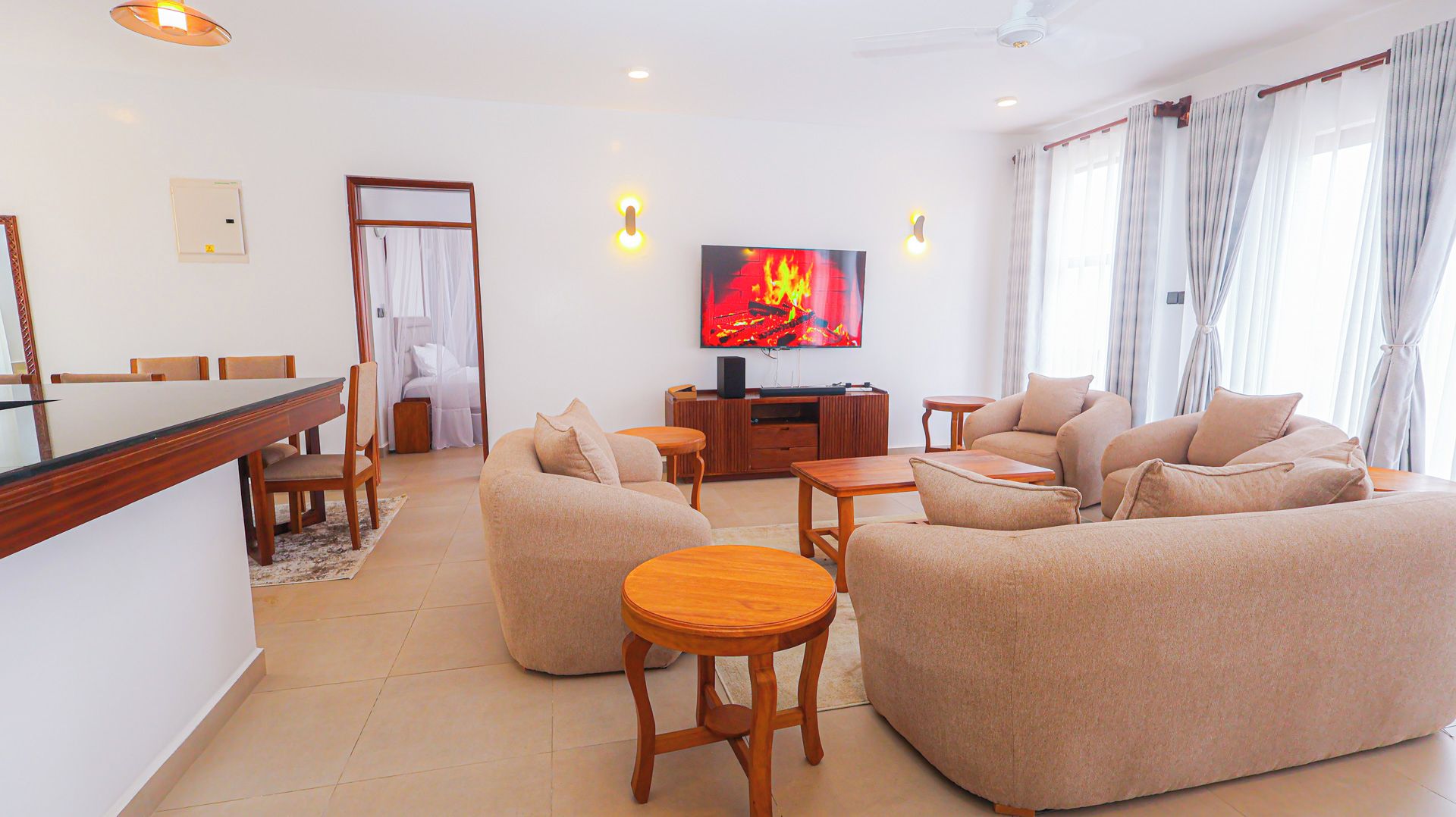 Una sala de estar moderna con un televisor de pantalla plana, sofás color beige, una mesa de centro de madera y un comedor con sillas.