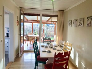 Un comedor con una mesa dispuesta para cuatro, sillas y vistas al jardín a través de grandes ventanales.